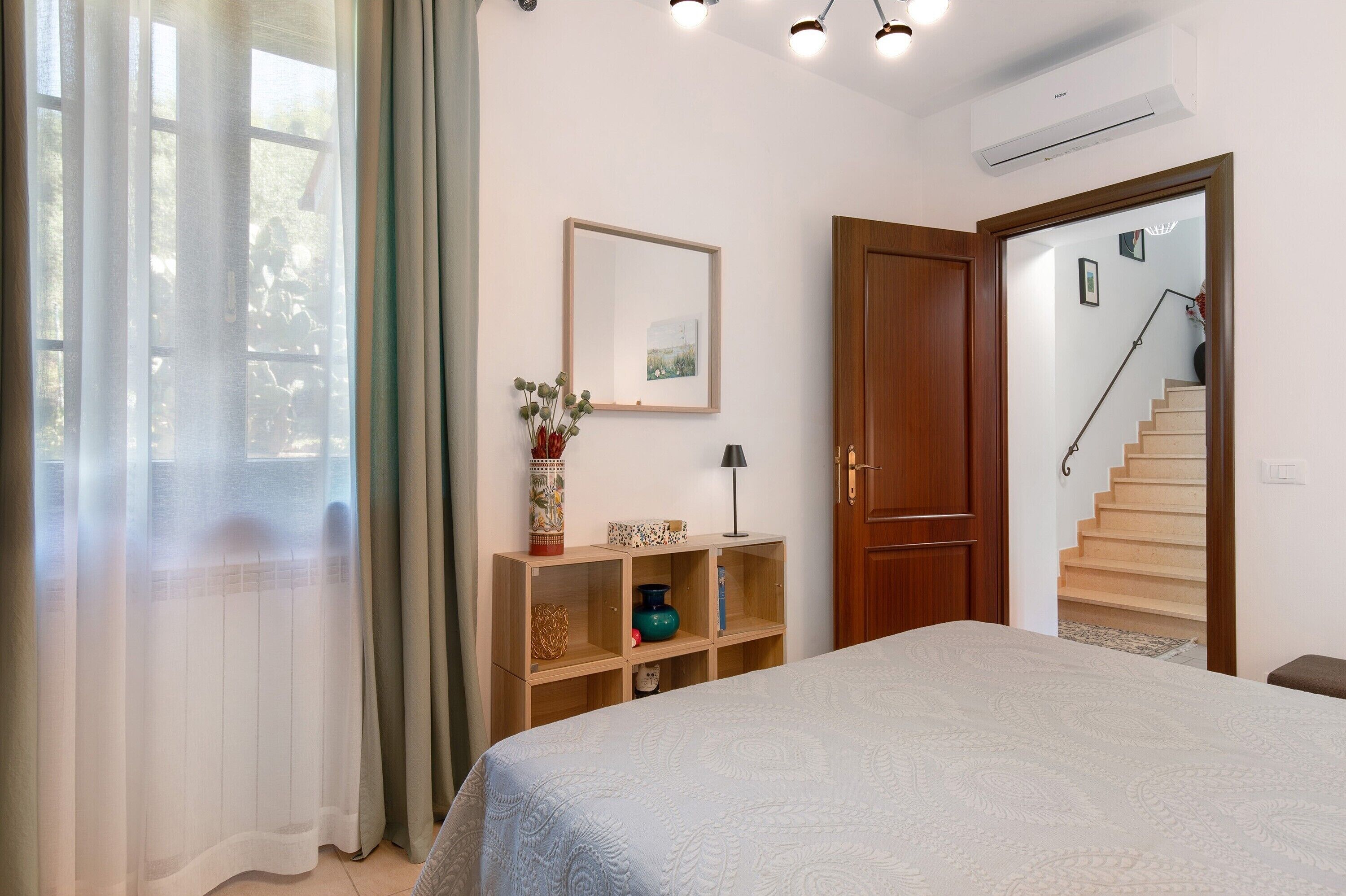 Ein Schlafzimmer mit einem Bett, einer Holzablage mit Dekoration, einem Spiegel und einer Treppe, die in einen anderen Raum führt.