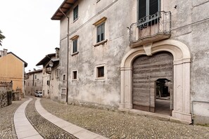 Une ruelle étroite pavée, bordée d’un immeuble remarquable avec une grande porte en arc de cercle et un balcon orné de balustrades en fer forgé.