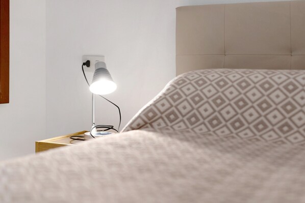 A bed with a patterned pillow, a bedside lamp, and a wooden nightstand.