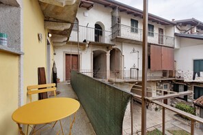 A courtyard with a yellow table, a green screen, and a building with balconies and a wooden door.