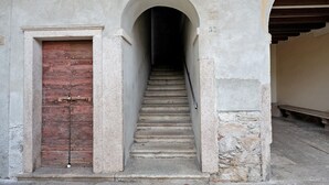 A stone staircase leading to a wooden door with a metal lock, flanked by arches and a stone wall.