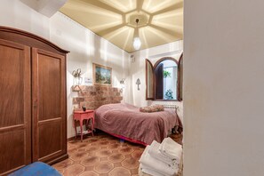 Un dormitorio con cama, armario, una mesita, lámpara y ventana con persianas.