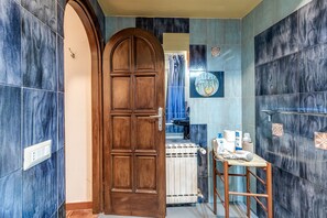 Un baño con puerta de madera, azulejos azules, un perchero y un radiador.