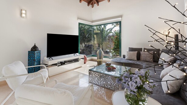 A modern living room with a flat-screen TV, white sofas, a glass coffee table, and a large window with a view of greenery. - El Refugio Vacation Home with Mountain Views, Private Pool, and Wi-Fi (La Oliva)