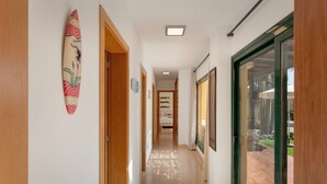 A hallway with wooden doors, a surfboard decoration, framed pictures, and a glass door leading to an outdoor area. - El Refugio Vacation Home with Mountain Views, Private Pool, and Wi-Fi (La Oliva)