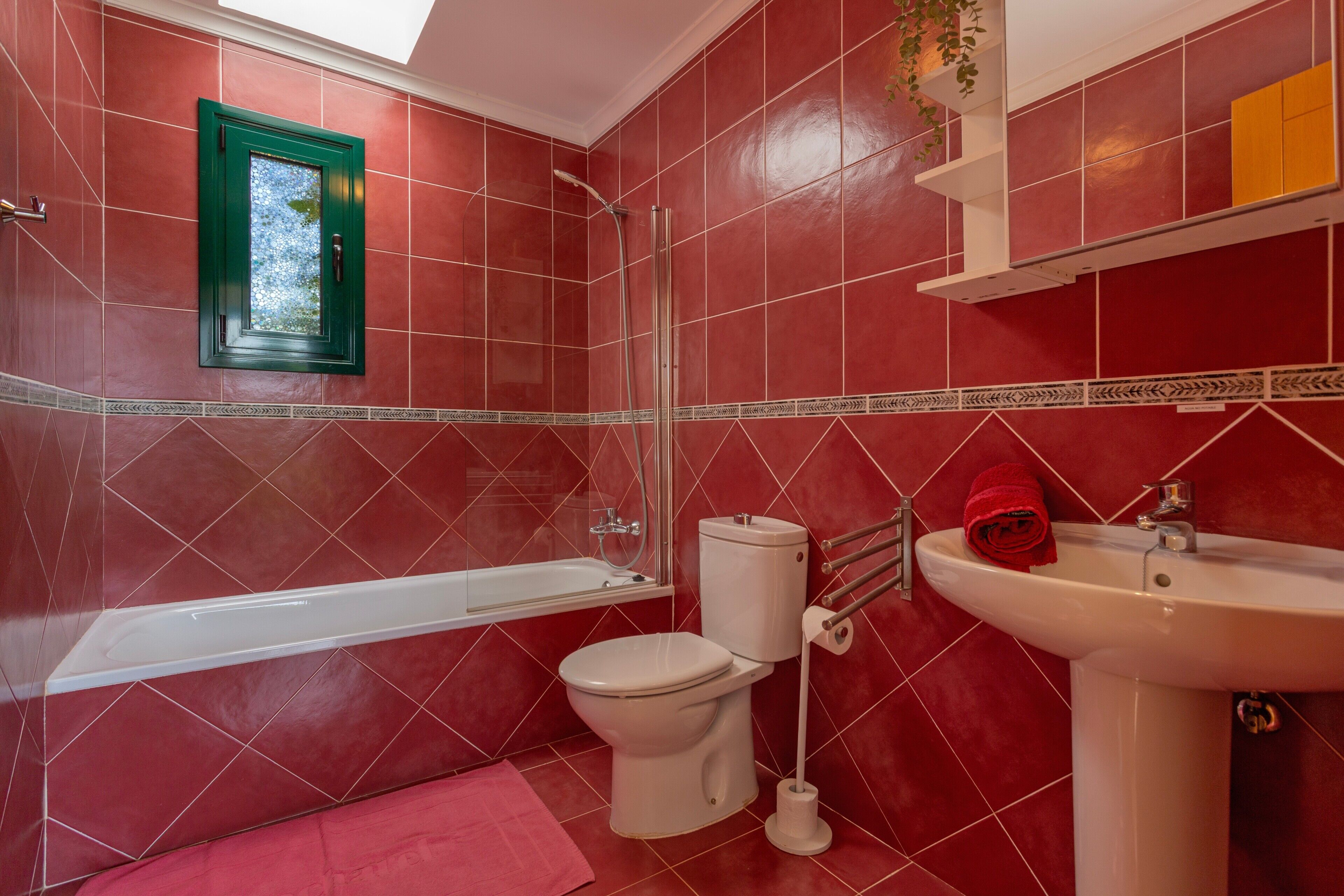A bathroom with red tiles, a white bathtub, a toilet, and a sink.