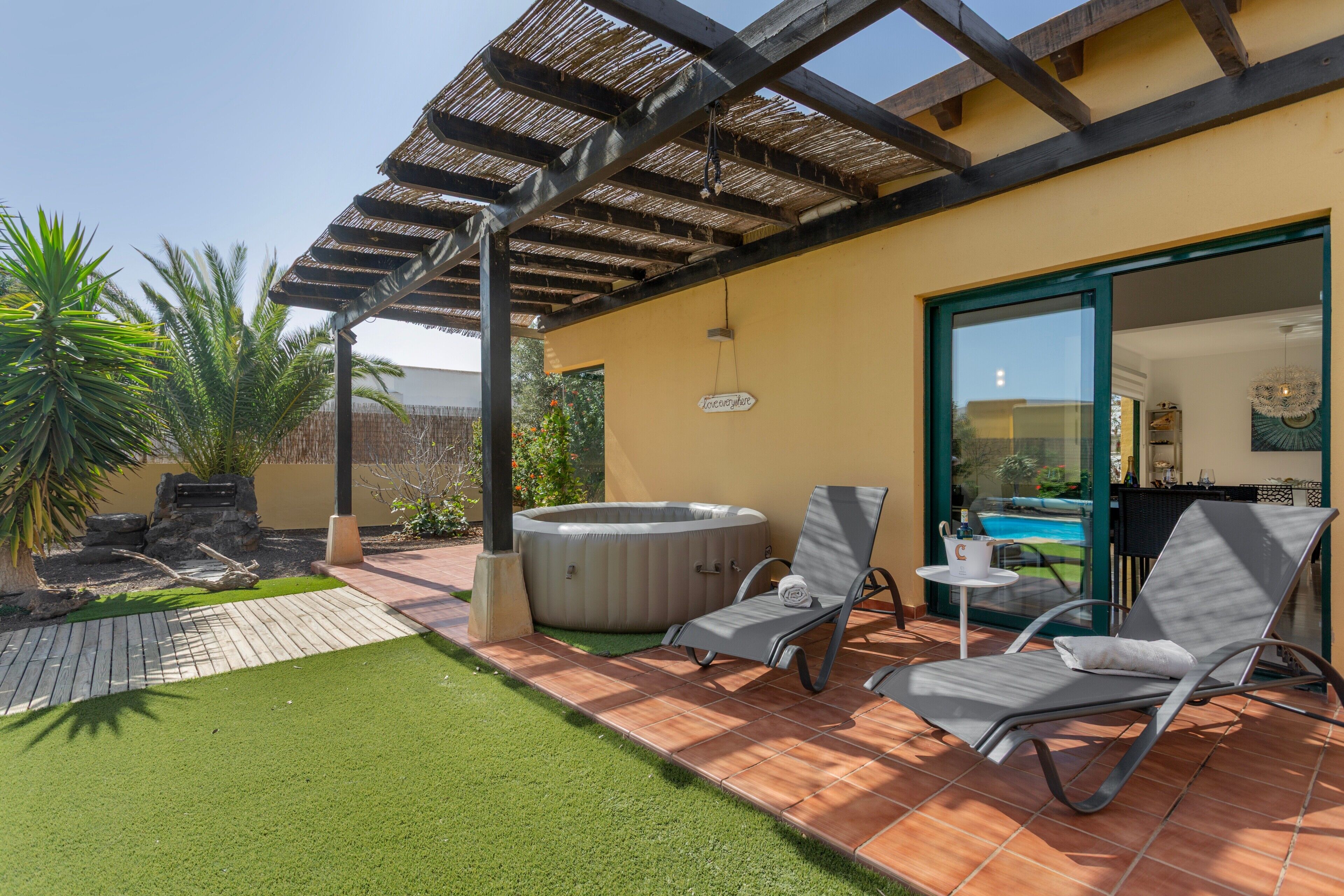 Une terrasse dotée d’un jacuzzi, de deux chaises longues, d’une pergola et d’une petite table.