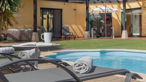 A poolside area with lounge chairs, a table with a cup, and a neatly rolled towel. - El Refugio Vacation Home with Mountain Views, Private Pool, and Wi-Fi (La Oliva)