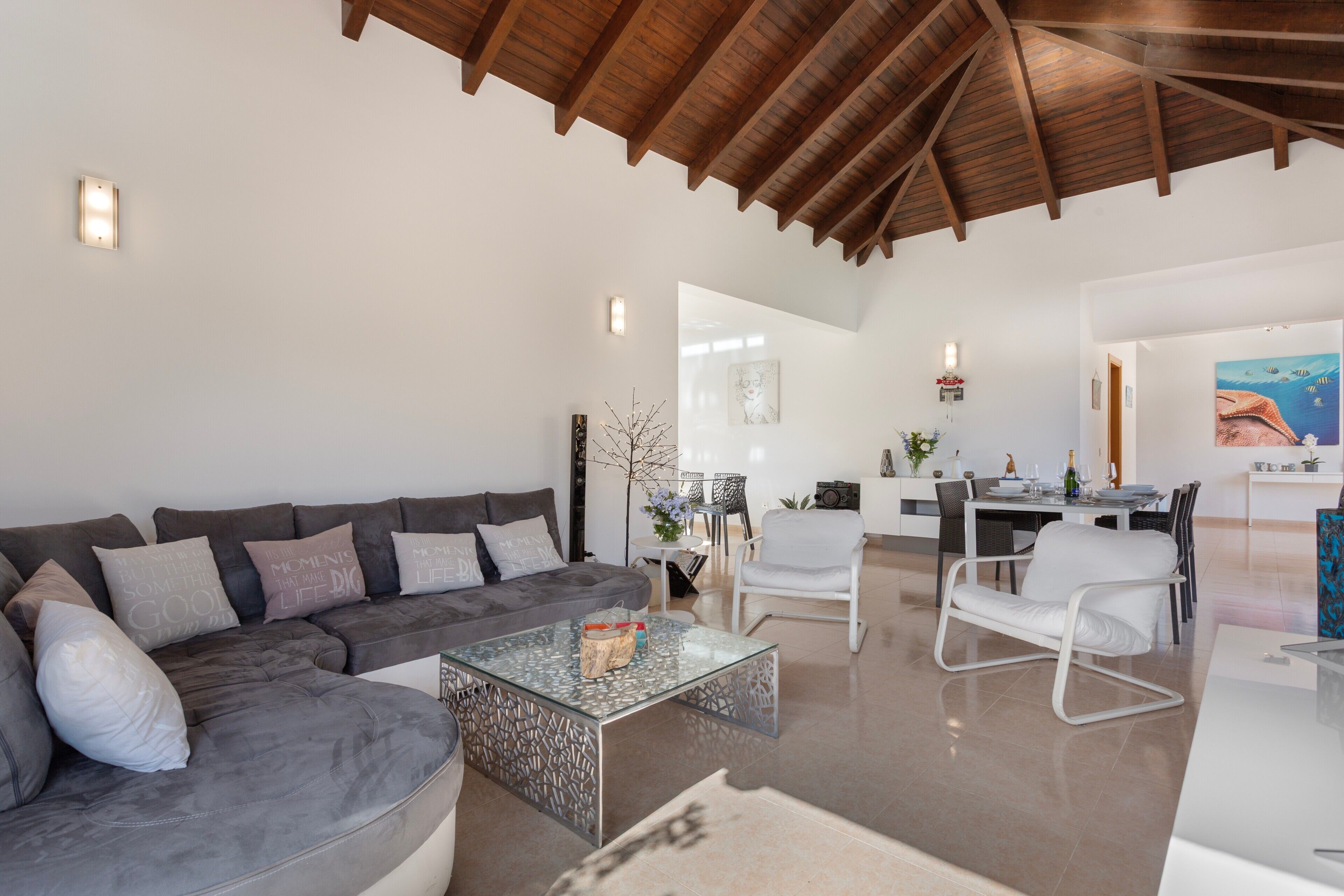 A spacious living area with a modern sofa, a glass coffee table, and a dining area with a white chair and table.