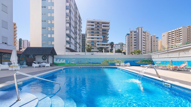 Una piscina con escalera metálica, sillones de descanso y un mural en la pared.