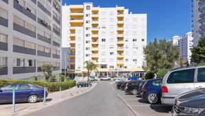 Un edificio residencial de varios pisos con balcones, un estacionamiento con autos y un cielo azul despejado.