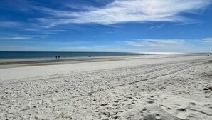 Uma extensa praia de areia com pegadas e um céu azul límpido.