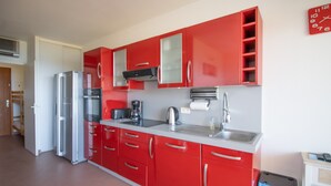 Una cocina con gabinetes rojos, un refrigerador de acero inoxidable, un microondas, un lavamanos y un reloj en la pared.