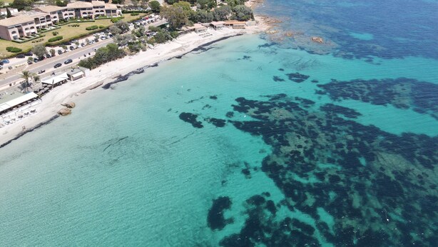 Vista aérea de una zona costera con edificios, una playa y aguas azules cristalinas.