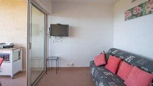 Una sala de estar con sofá, televisor, una mesita y una kitchenette.