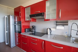 Une cuisine moderne avec des meubles de rangement rouges, un réfrigérateur en acier inoxydable, une machine à café et une bouilloire.