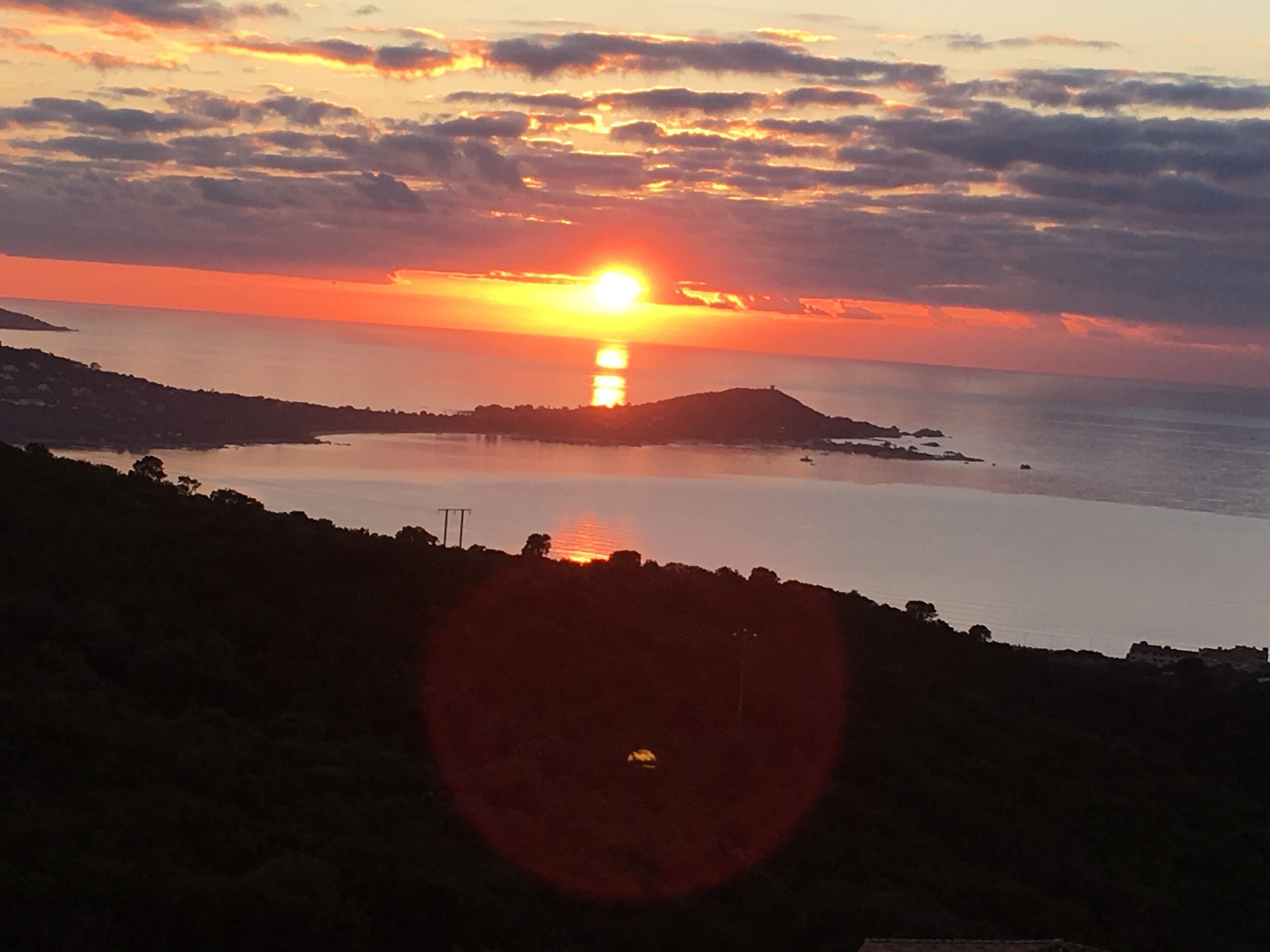 Een zonsondergang boven een kalm wateroppervlak met verre landschappen.