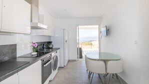 A modern kitchen with a built-in washing machine, a dining area with a glass table, and a view of the outdoors. - Apartment 'Superbe Neuf Climatisé' with Sea View, Wi-Fi and Air Conditioning (Albitreccia)