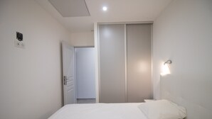 A bedroom with a bed, a wardrobe, and a wall-mounted light fixture. - Apartment 'Superbe Neuf Climatisé' with Sea View, Wi-Fi and Air Conditioning (Albitreccia)