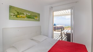 A bedroom with a bed, a red blanket, a painting, and a view of the outdoors. - Apartment 'Superbe Neuf Climatisé' with Sea View, Wi-Fi and Air Conditioning (Albitreccia)