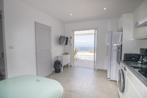 A modern kitchen with a washing machine, a TV mounted on the wall, and a view of the sea through an open door. - Apartment 'Sublime Neuf' with Sea View, Shared Pool and Wi-Fi (Albitreccia)