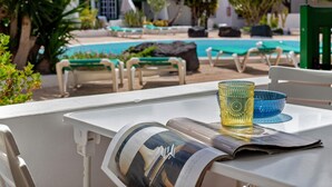 Un área junto a la piscina con sillas de descanso, una mesa de vidrio y una revista.