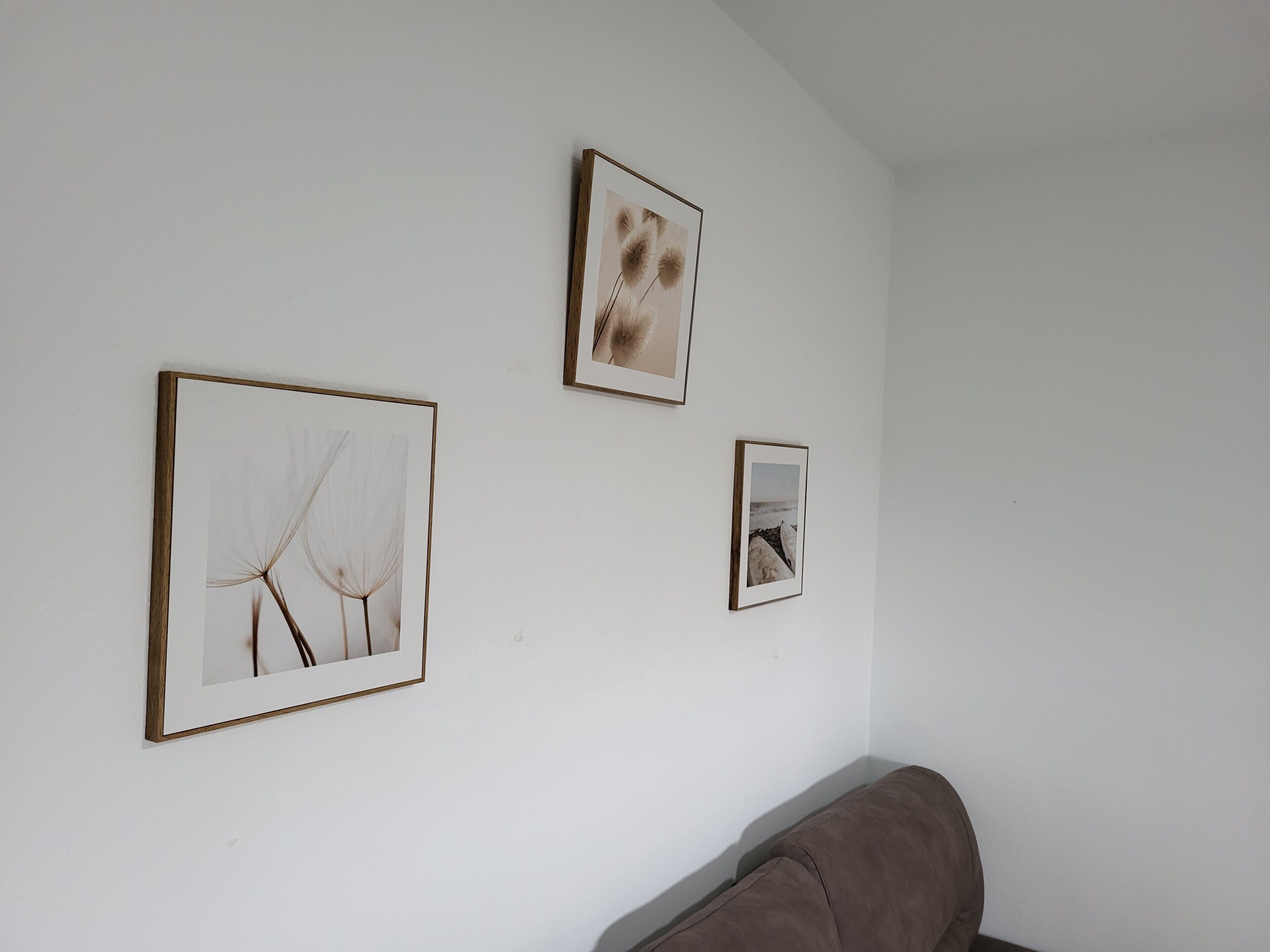 Una habitación con una pared blanca, un sofá marrón y tres cuadros enmarcados.