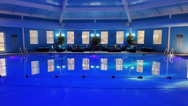 Une piscine intérieure avec un plafond et des murs bleus, entourée d’espaces aménagés pour s’asseoir et de plantes en pot.