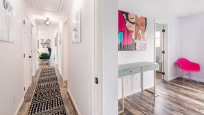 Un couloir moderne avec un tapis à motifs, un fauteuil vert et un bureau doté de tiroirs.