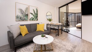 A modern living room with a grey sofa, yellow cushions, a white coffee table, and a flat-screen TV mounted on the wall.