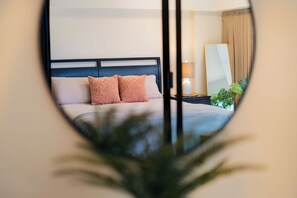 A hotel room with a bed, a nightstand, a lamp, a mirror, and a plant.