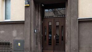 Ruskeat pariovet, joiden yläpuolella on pieni ikkuna, ovikello ja kyltti oven yläpuolella.
