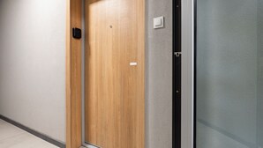 Una puerta de madera con un picaporte moderno y un pequeño panel de control, junto a un muro de cristal.