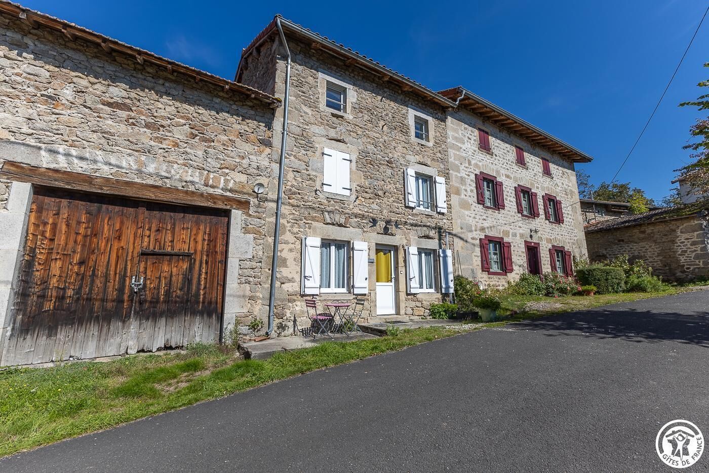 A two-story stone building with a garage, a small outdoor seating area, and a clear sky.
