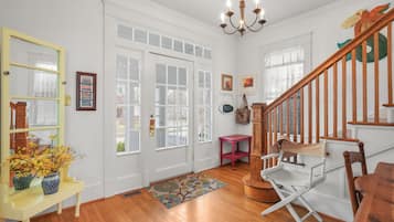Une pièce spacieuse dotée d’un parquet, d’un escalier en bois, d’un banc, d’une chaise de réalisateur et d’un lustre.