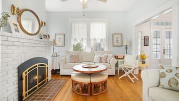 Un salon avec une cheminée, une table basse ronde en bois, un canapé blanc et un fauteuil blanc.