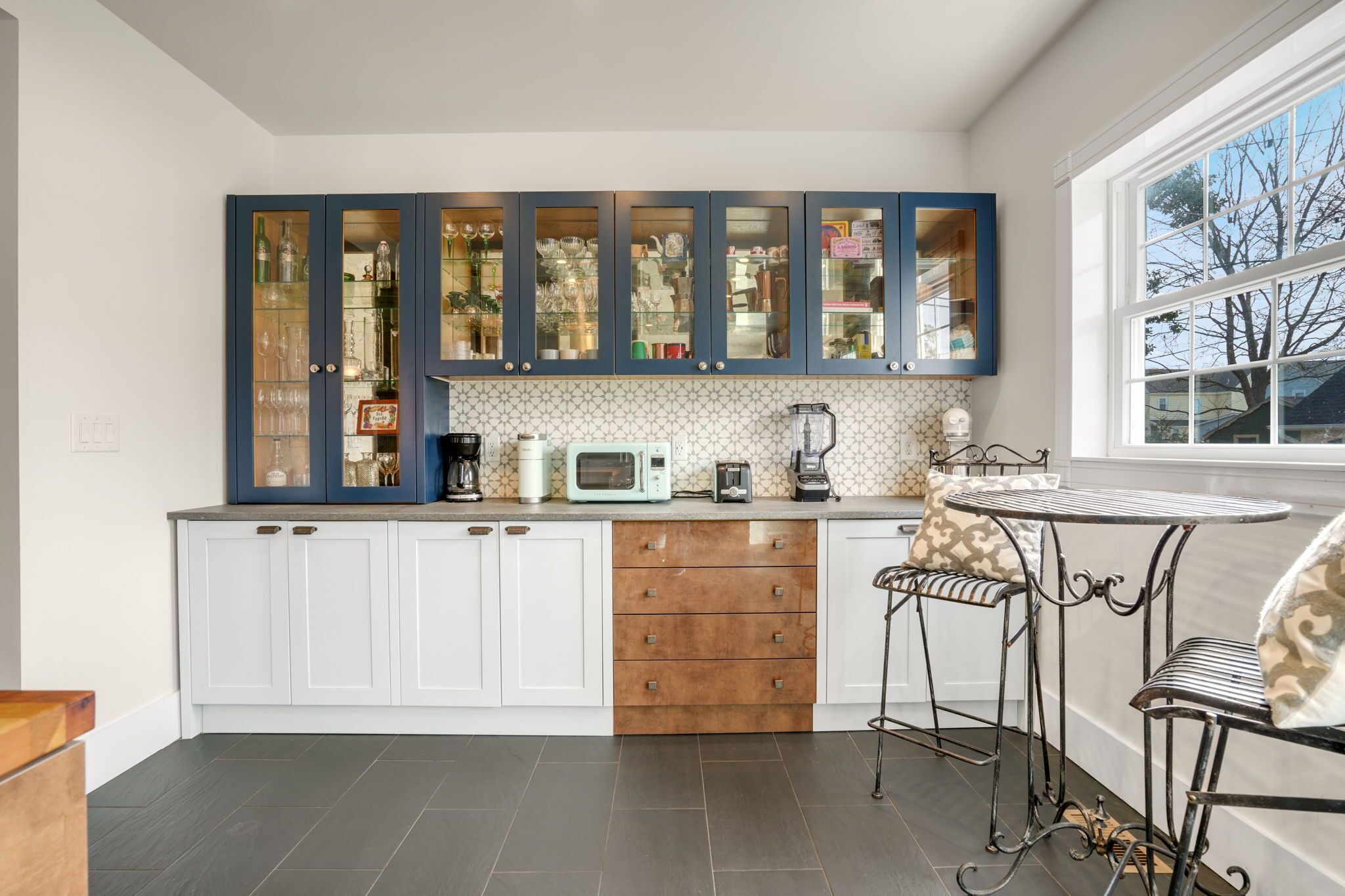 A kitchen with white cabinets, a microwave, a coffee maker, and a window with a view of trees.