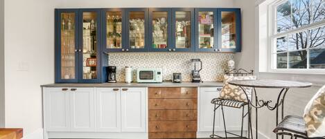 A kitchen with white cabinets, a microwave, a coffee maker, and a window with a view of trees.