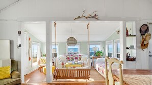 Un vaste espace de vie comprenant une table à manger en bois, un canapé et un banc. De nombreuses fenêtres laissent entrer la lumière naturelle et offrent une vue sur l’extérieur.