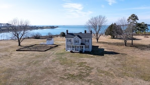 Une maison à deux étages avec une grande véranda à l’avant, une cour clôturée et une vue sur un lac.