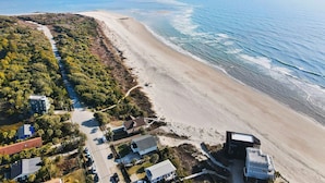 Ein Luftbild einer Küstenregion mit Strand, einer Straße und mehreren Gebäuden, darunter eine große, blaue Struktur mit Flachdach.