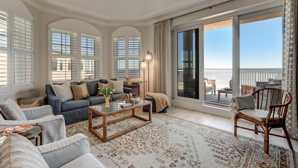A spacious living room with a large sofa, a coffee table, and a view of the balcony.