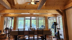 Una stanza spaziosa con soffitto alto, travi in legno, ventilatore a soffitto e ampie finestre che danno su un panorama esterno.