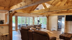 Un'ampia zona giorno con soffitto in legno, un divano grande, un tavolo da pranzo con sedie e una cucina visibile attraverso una porta aperta.