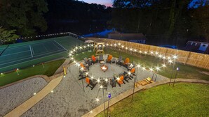 An outdoor seating area with a fire pit, surrounded by chairs and tables, and string lights.