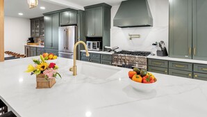A modern kitchen with dark green cabinets, a white marble countertop, and stainless steel appliances.