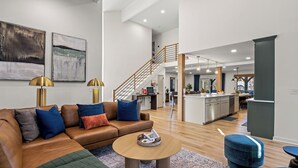 A spacious living area with a brown leather sofa, a round coffee table, and a blue ottoman. A staircase leads to an upper level.