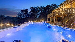 A hot tub area with a wooden deck and string lights, surrounded by trees.