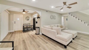 Un vaste salon avec un canapé beige, un coin repas comprenant une table et des chaises, un escalier et un ventilateur de plafond.
