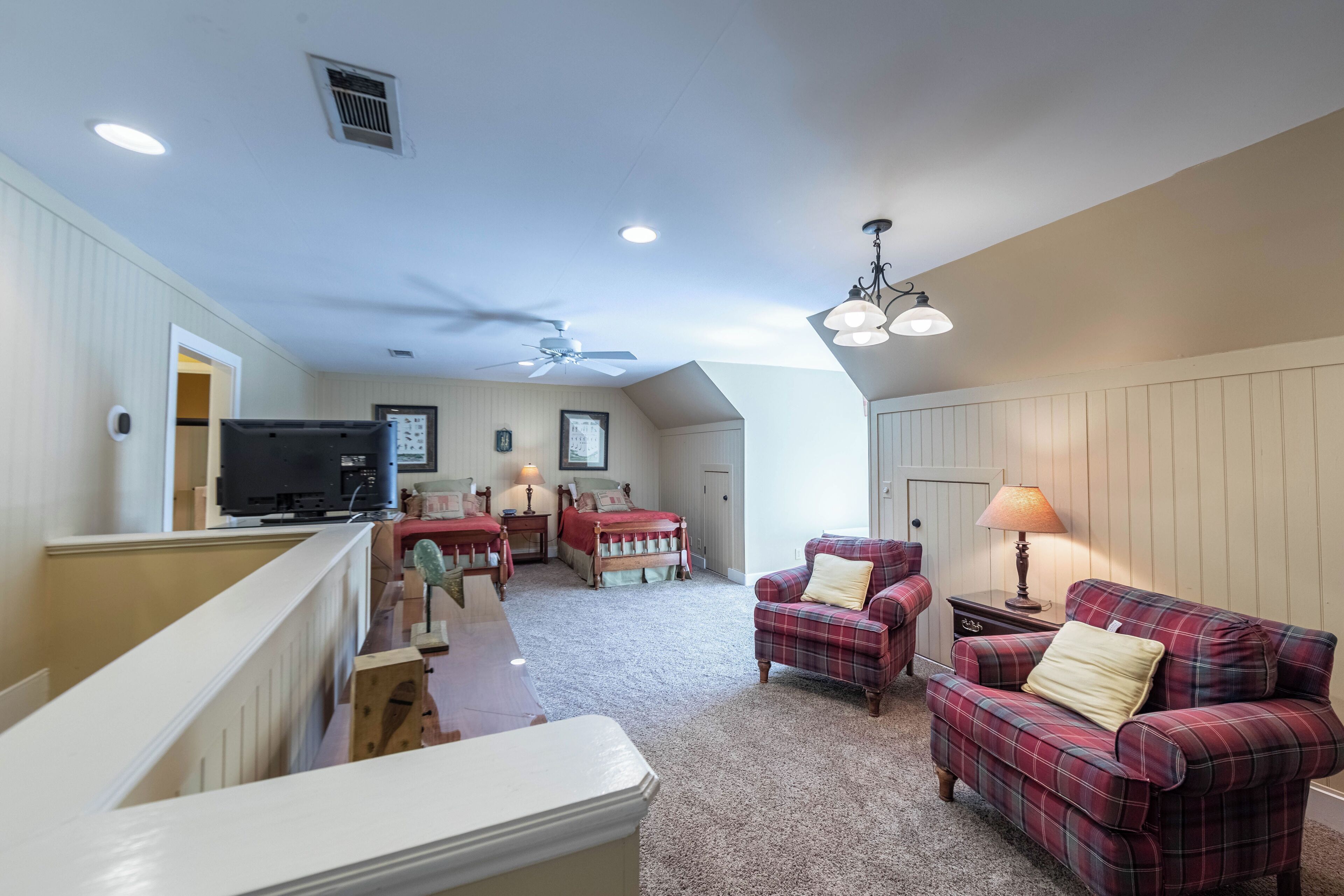 A spacious living room with a high ceiling, a ceiling fan, and a fireplace. There is a red plaid sofa and a wooden coffee table.